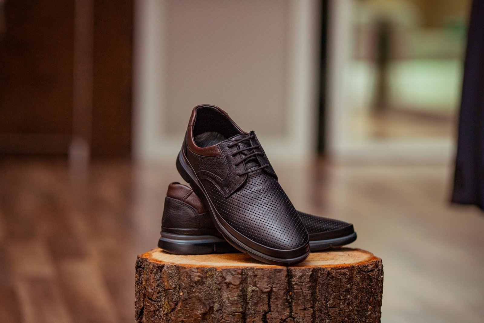 Stylish perforated leather shoes displayed elegantly on a rustic wooden stump indoors.